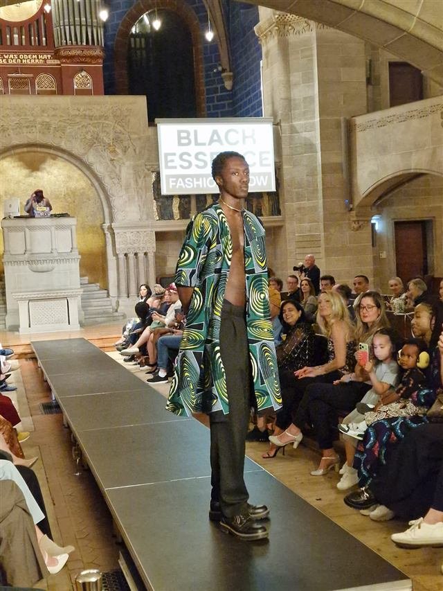 Model in a green and teal patterned coat on the runway at the Black Essence Fashion Show in Basel